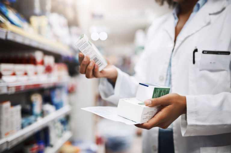 Pharmacist in white coat holding two medicine boxes in one hand and one medicine box in other